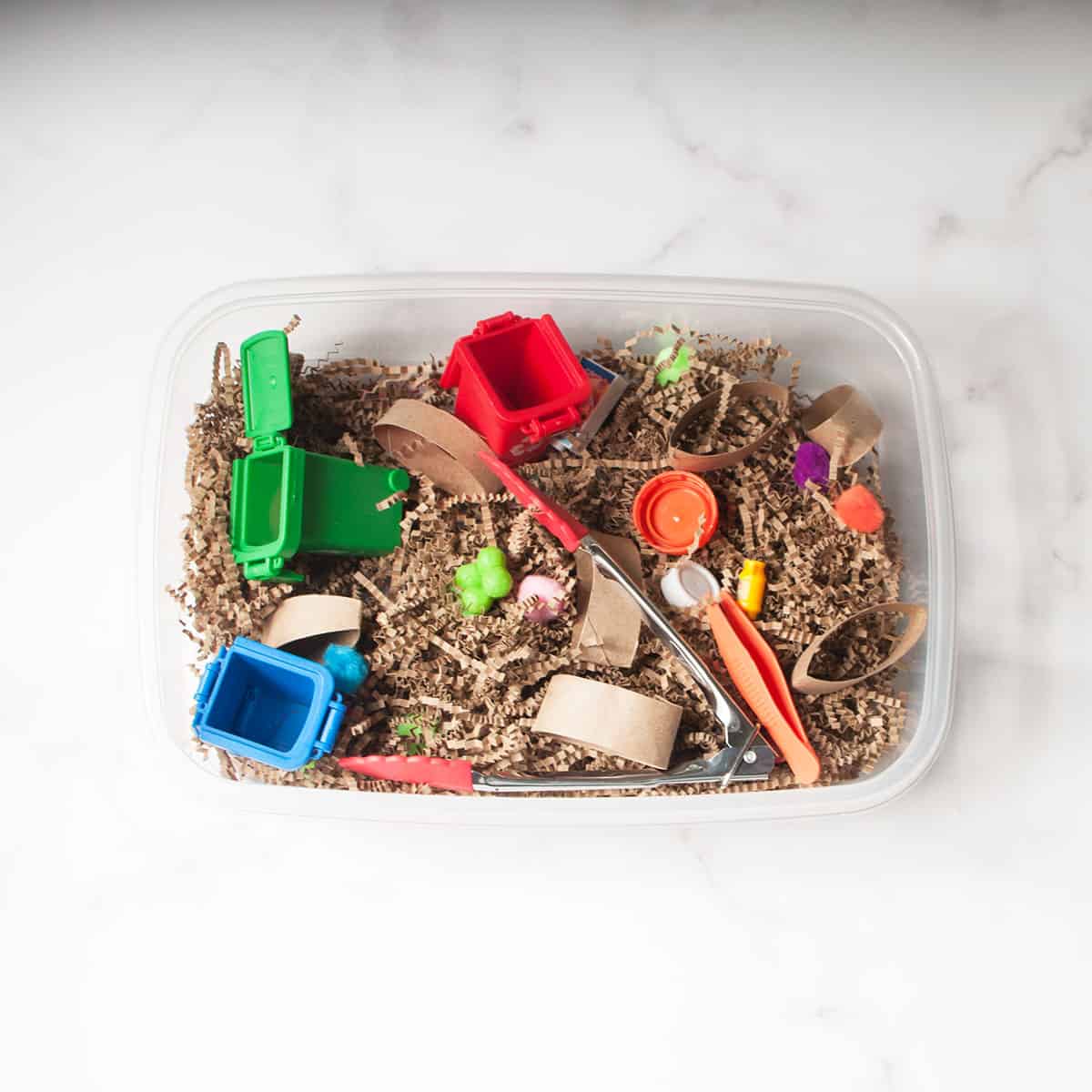 A sensory bin with a recycling theme. It is made from brown crinkle paper, scoops, toys, and recyled household items.