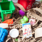 A sensory bin with a recycling theme. It is made from brown crinkle paper, scoops, toys, and recyled household items.