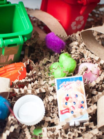 A sensory bin with a recycling theme. It is made from brown crinkle paper, scoops, toys, and recyled household items.
