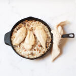 Chicken and rice in a cast iron skillet. The skillet has a linen tea towel tied around the handle.