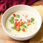 White queso (cheese dip) in a white bowl with cilantro and tomato on top.