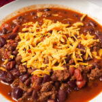Chili in a white bowl with shredded cheese on it.