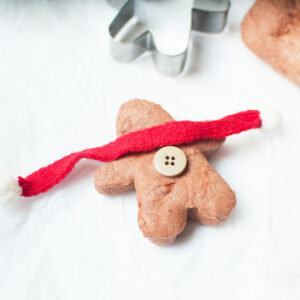 No cook gingerbread play dough shaped into a gingerbread man with a button and toy scarf.