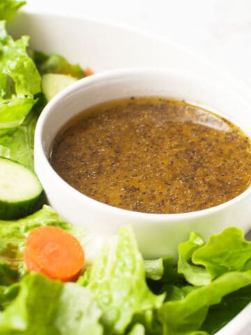 A bowl of Amish salad dressing surrounded by a salad with lettuce, cucumber, and carrot.