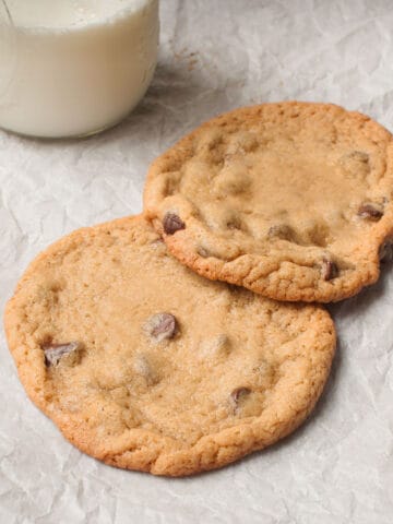 Two large chocolate chip cookies with a glass of milk on a white background.