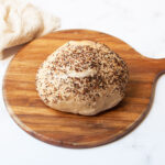 A loaf of Everything Bagel Sourdough bread on a wooden tray.