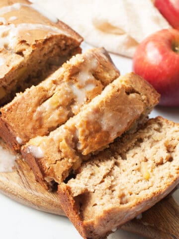 A photo of sourdough apple bread on a wooden tray with apples behind it.