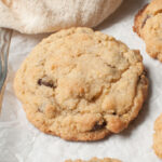 An upclose photograph of a chunky chocolate chip cookie. There is a cream linen behind it.