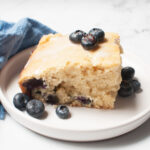 A slice of Sourdough Blueberry Coffee Cake on a plate with blueberries around it.