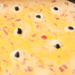 A close up photo of Halloween cheese dip with cheese and olive eyes in it.