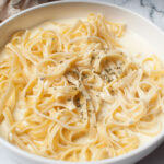 A white bowl with fettuccine and alfredo sauce.