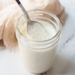 Copycat Carrabba's creamy parmesan salad dressing in a mason jar with a spoon in it. There is a cream linen behind it.