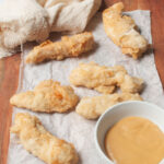 Chicken tenders with a dipping sauce on a wooden board.