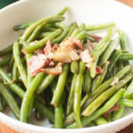 Close up image of green beans with bacon pieces on top of them.