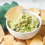 Copycat Qdoba guacamole in a white dish surrounded by tortilla chips.