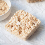 A brown sugar rice crispy treat on a white background next to a small bowl of brown sugar.