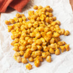 Pan fried chickpeas with turmeric on a piece of parchment paper with an orange linen behind them.