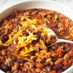 A bowl of crockpot turkey chili with a spoon in it and shredded cheese on top.