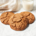 Amish Molasses Cookies on a white background with a glass of milk behind them.