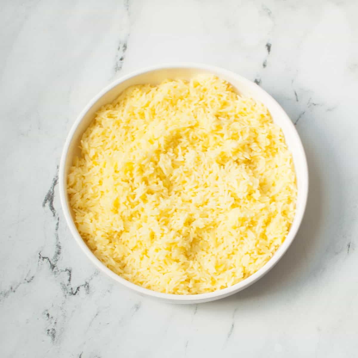 Copycat Cava Saffron Rice in a white bowl on a marble background.