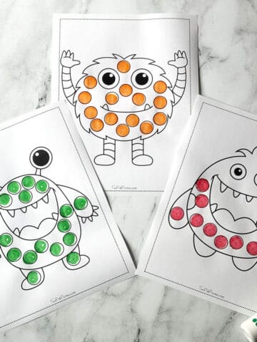 A photograph of three monster dot marker pages on a marble background.