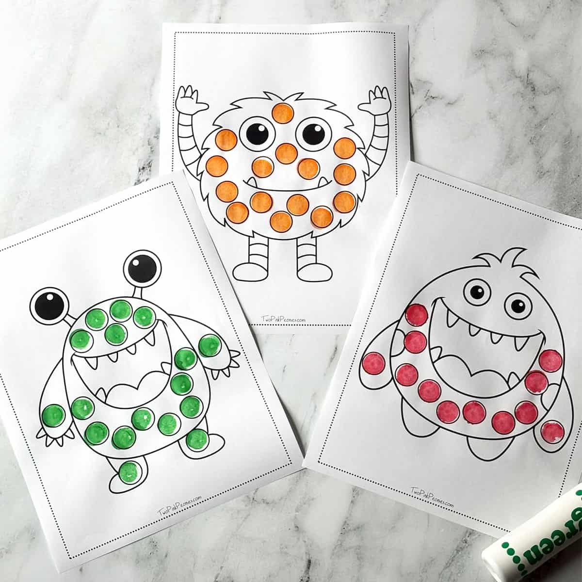 A photograph of three monster dot marker pages on a marble background.