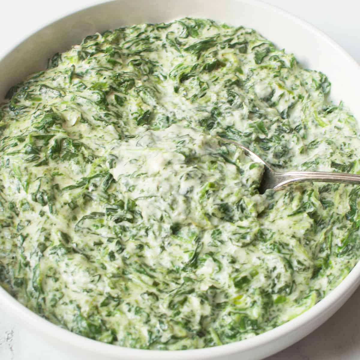 Copycat Boston Market Creamed Spinach in a white bowl with a spoon.