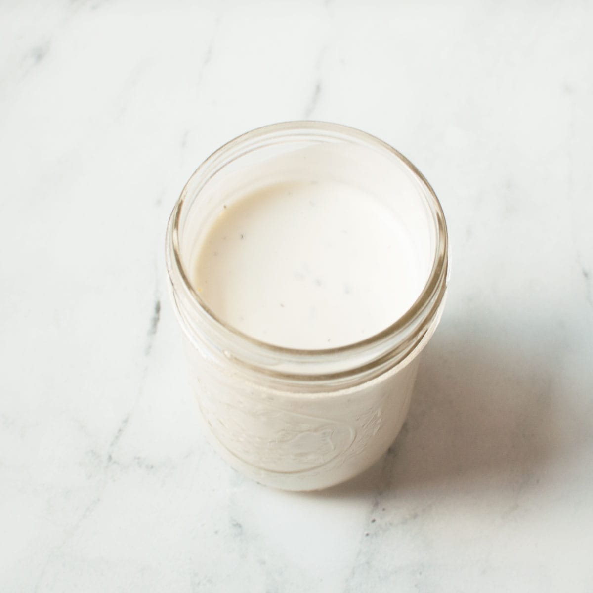 A photograph of copycat Creamy Parmesan Salad Dressing in a mason jar on a marble background.