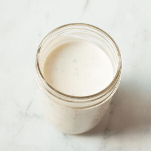 A photograph of copycat Creamy Parmesan Salad Dressing in a mason jar on a marble background.