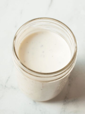 A photograph of copycat Creamy Parmesan Salad Dressing in a mason jar on a marble background.