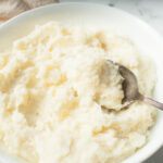 Copycat Texas Roadhouse Mashed Potatoes in a white bowl with a spoon in them.