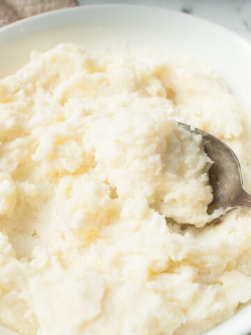 Copycat Texas Roadhouse Mashed Potatoes in a white bowl with a spoon in them.