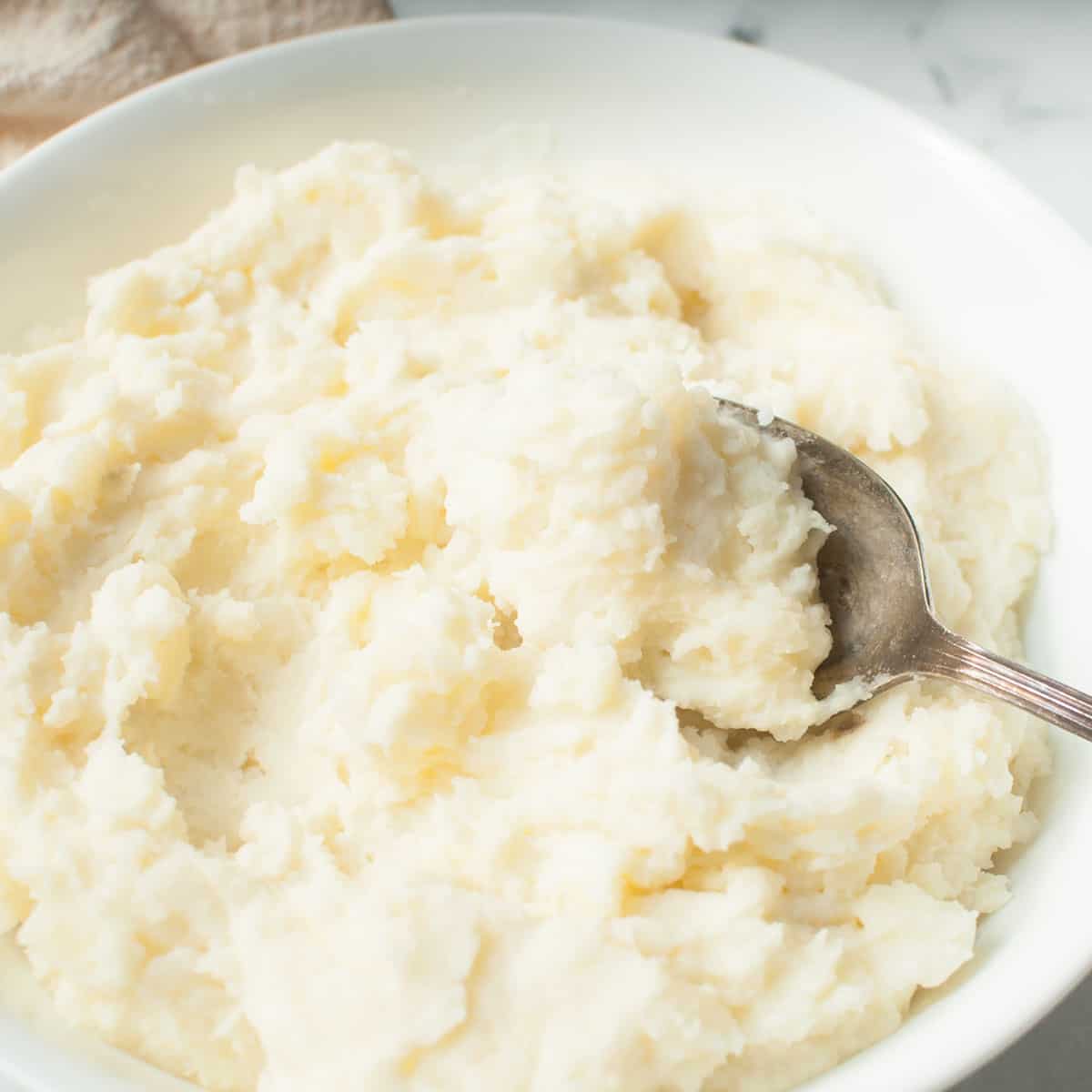 Copycat Texas Roadhouse Mashed Potatoes in a white bowl with a spoon in them.