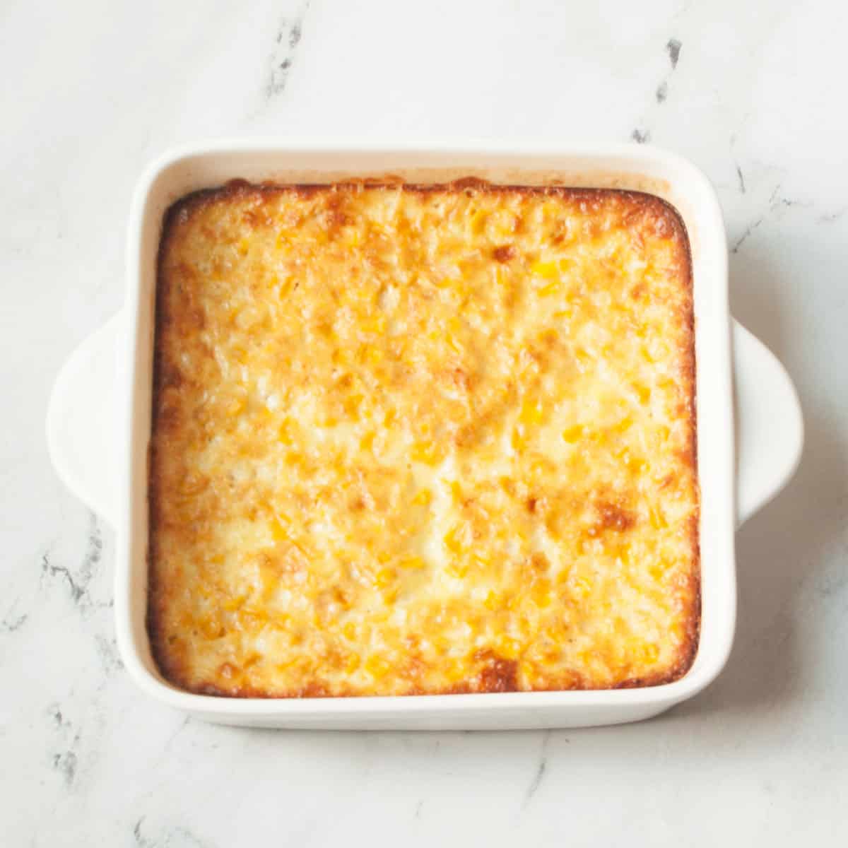 Corn pudding in a white casserole dish on a marble background.